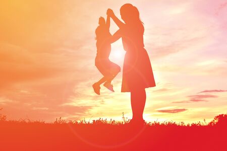 silhouettes mother and little daughter playing at sunsetの写真素材