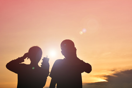 Silhouette boy and girl with smartphone at sunsetの写真素材