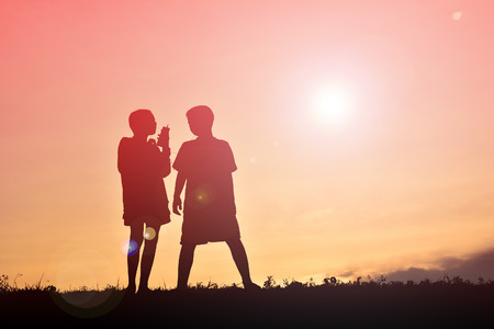 Silhouette boy and girl with smartphone at sunsetの写真素材