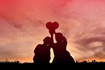 Silhouette mother and son holding heart shape at sunsetの写真素材