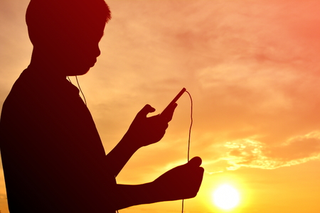 Silhouette boy with smartphone at sunsetの写真素材
