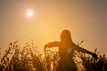 Silhouette of happy women open hand in grass field at the sky sunsetの写真素材