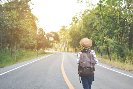 Happy Asian girl backpack  in the road and forest background, Relax time on holiday concept travel ,color of vintage tone and soft focusの写真素材