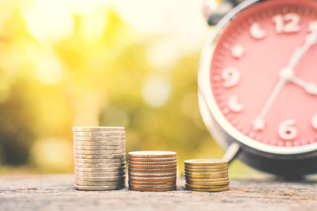 coin with alarm clock on old wood and tree bokeh background , a color of vintage tone concept save moneyの写真素材