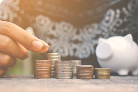 Hand of women holding coin to set money and white piggy bank on old wood background ,vintage toneの写真素材