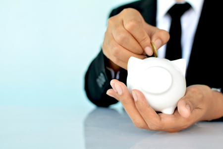 Businesswomen holding coin and white piggy bank on blue background selective and soft focusの写真素材