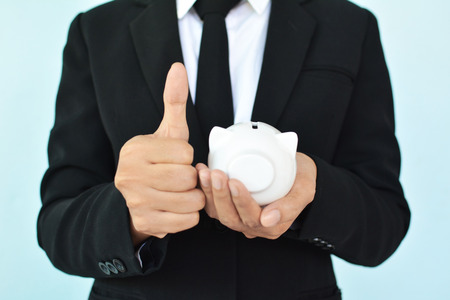 Businesswomen holding coin and white piggy bank on blue background selective and soft focusの写真素材