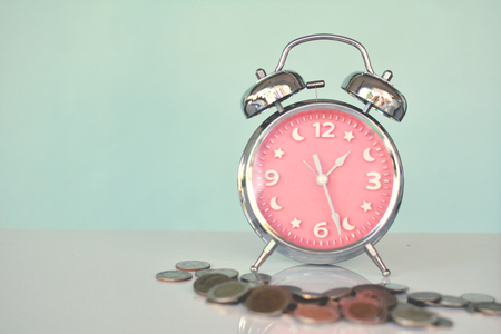 Alarm clock with coin on table in blue backgroundの写真素材