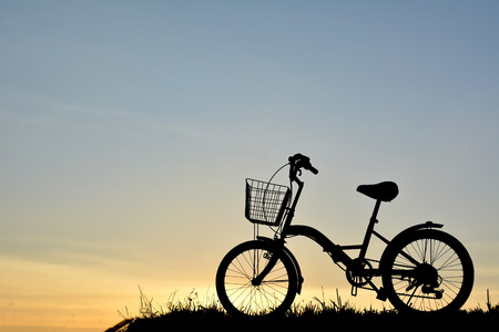Silhouette of bicycle on grass with the sky sunsetの写真素材