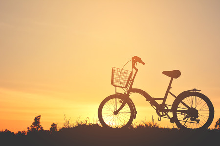 Silhouette of bicycle on grass with the sky sunsetの写真素材