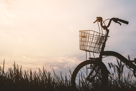 Silhouette of bicycle on grass with the sky sunsetの写真素材