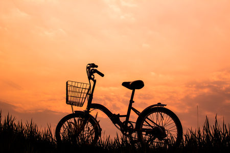 Silhouette of bicycle on grass with the sky sunsetの写真素材