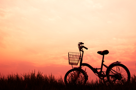 Silhouette of bicycle on grass with the sky sunsetの写真素材