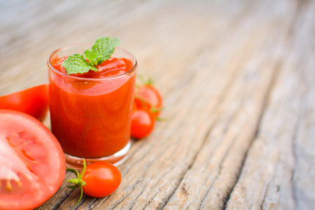 tomato sauce in a glass and fresh tomatoes on old woodの写真素材
