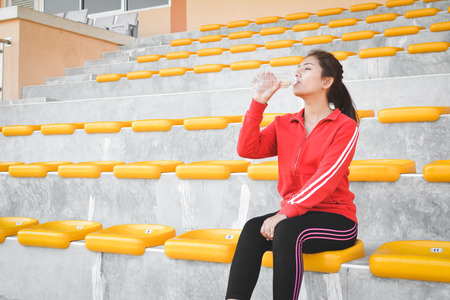 Young women drinking water after exercise in stadium