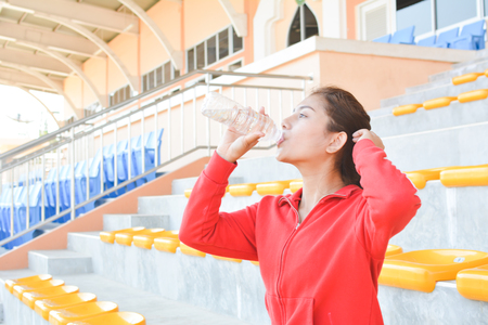 Young women drinking water after exercise in stadiumの写真素材