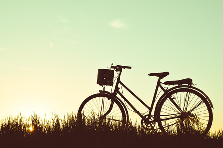 Silhouette of old bicycle on grass with the sky sunset, color of vintage tone and soft focus concept journeyの写真素材