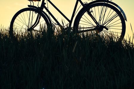 Silhouette of old bicycle on grass with the sky sunset, color of vintage tone and soft focus concept journeyの写真素材