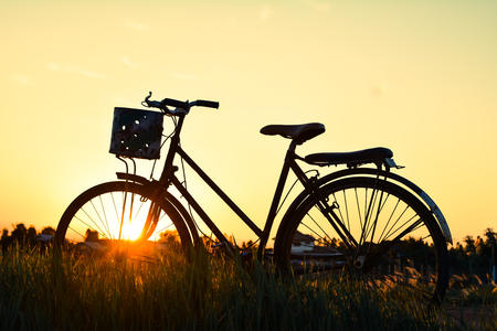 Silhouette of old bicycle on grass with the sky sunset, color of vintage tone and soft focus concept journeyの写真素材