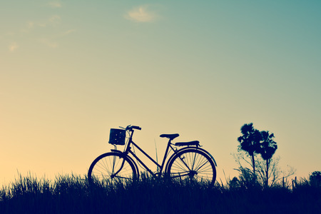 Silhouette of old bicycle on grass with the sky sunset, color of vintage tone and soft focus concept journeyの写真素材