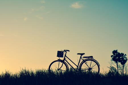 Silhouette of old bicycle on grass with the sky sunset, color of vintage tone and soft focus concept journeyの写真素材