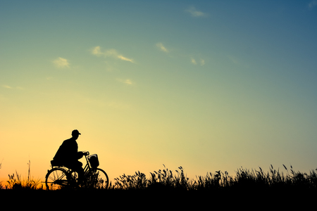 Silhouette of man and old bicycle on grass with the sky sunset, color of vintage tone and soft focus concept journeyの写真素材