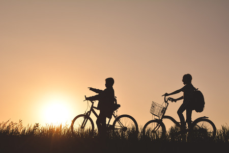 Silhouette of children with bicycle on grass field at the sky sunset, color of vintage tone and soft focus concept journey in holidayの写真素材