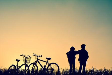 Silhouette of children with bicycel on grass field at the sky sunset, color of vintage tone and soft focus concept journey in holidayの写真素材