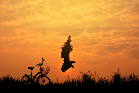Silhouette of girl with bicycle on grass field at the sky sunset, color of vintage tone and soft focus concept journeyの写真素材