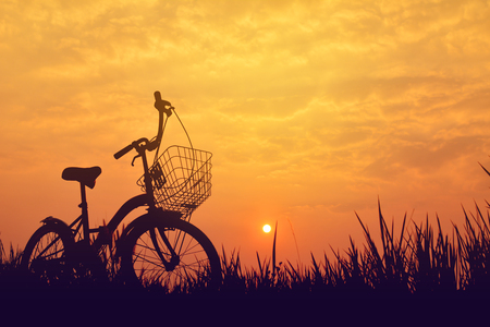 Silhouette of bicycle on grass with the sky sunsetの写真素材