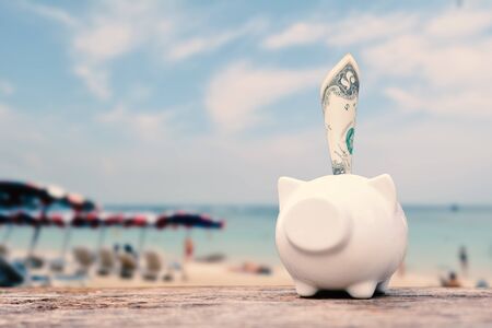 Piggy bank and money on table and sea background, concept save money to travelの写真素材