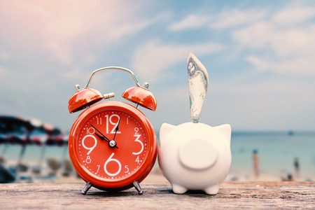Piggy bank and alarm clock on table and sea background, concept save money to travelの写真素材