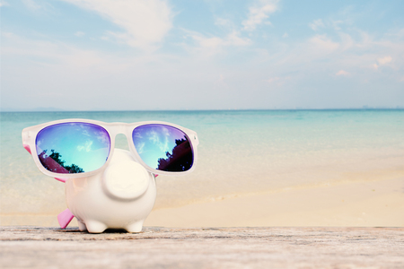 Piggy bank and sunglass on table and sea background, concept save money to travelの写真素材