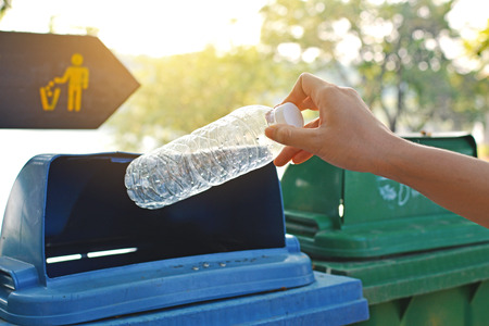 Close up hand holding empty bottle into the trashの写真素材