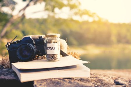 Close up coin on glass jar with travel word and accessories for backpack on stone nature background, color vintage toneの写真素材