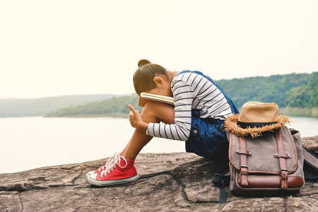 Happy Asian girl reading a book in nature background, Relax time on holiday, color of vintage tone and soft focusの写真素材