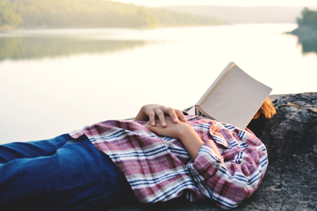 Girl sleeping with book near river and nature background , color vintage selective and soft focusの写真素材