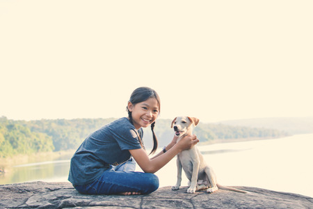 Happy girl playing with little dog in nature background, travel on holiday color of vintage toneの写真素材