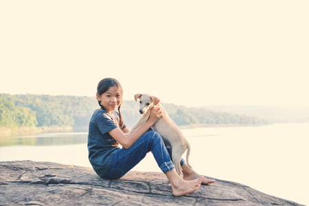 Happy girl playing with little dog in nature background, travel on holiday color of vintage toneの写真素材