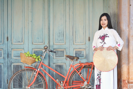Beautiful women Vietnam with white Ao Dai dress and red bicycle in old city , selective and soft focus of face color vintage styleの写真素材