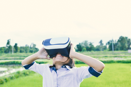 Asian girl playing VR virtual reality glass box outdoor in grass field ,color of vintage style and soft focusの写真素材