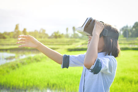 Asian girl playing VR virtual reality glass box outdoor in grass field ,color of vintage style and soft focusの写真素材