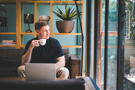 Happy handsome young man drinking coffee with using computer in cafe shop relax time on holiday ,color of hipster style selective and soft focusの写真素材