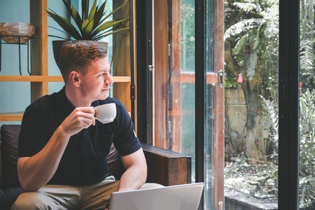 Happy handsome young man drinking coffee with using computer in cafe shop relax time on holiday ,color of hipster style selective and soft focusの写真素材
