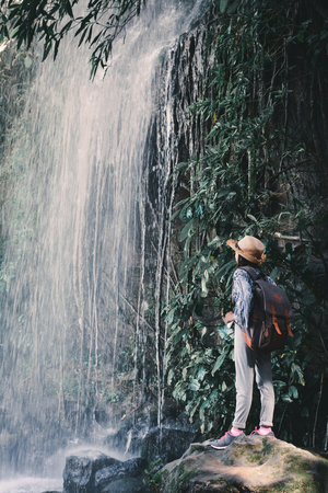 Happy Asian girl standing on stone and waterfall background , concept backpacker in the forestの写真素材