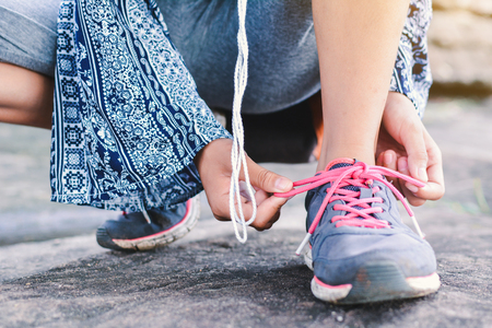 Close up girl hands tying shoelace on shoes during walkingの写真素材