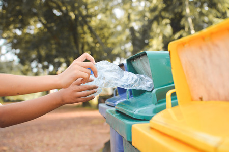 Close up children hand holding empty bottle into the trashの写真素材