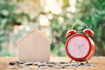 Coins and wood house with red alarm clock on table tree bokeh background concept save money for home ,selective and soft focus vintage toneの写真素材