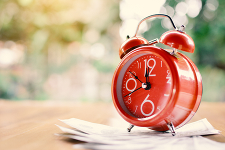 Red alarm clock and money on wood table tree bokeh backgroundの写真素材