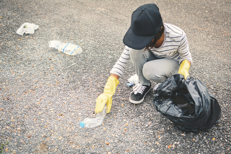 Girl hand in yellow gloves picking up empty of bottle plastic into bin bag ,volunteer conceptの写真素材